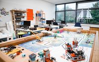 Ein Klassenzimmer mit mehreren Computern, Regalen und einem großen Tisch für Robotik- und Technikprojekte.