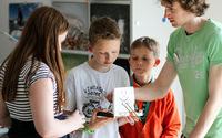 Schülerinnen und Schüler besprechen mit einem Betreuer ein selbst gebautes Boot