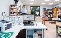 Arbeitsbereich in einem Schülerforschungszentrum mit Computern, 3D-Druckern und verschiedenen technischen Geräten.
