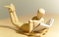 Auf dem Bauch liegende Holzfigur, die so positioniert ist, als würde sie ein Buch lesen.