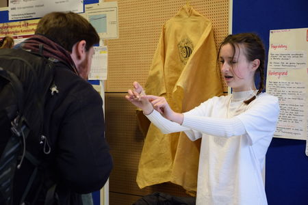 Eine junge Forscherin des Schülerforschungszentrums Kieler Forschungswerkstatt präsentiert einem interessierten Besucher ihr Material und erläutert die Funktionsweise auf einem Wettbewerb.