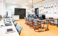 Der Computerraum des SFZs mit modernen Arbeitsplätzen, an denen Computer und Laptops aufgereiht sind, wartet auf die nächsten Schüler, die hier arbeiten werden. An der Wand im Hintergrund sind Tafelzeichnungen und Notizen zu sehen.