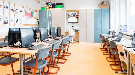Ein heller und gut ausgestatteter Computerraum mit aufgereihten Monitoren und Laptops wartet auf die nächsten Benutzer. Im Hintergrund sind Schränke, ein Mikroskop, und wissenschaftliche Poster zu sehen, die den Raum als einen Ort des Lernens und der Fors