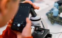 Nahaufnahme einer Person, die ein Smartphone verwendet, um ein Bild durch ein Mikroskop aufzunehmen.