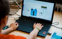 Ein Schüler arbeitet konzentriert an einem Laptop, auf dem ein Schaltplan für ein technisches Projekt angezeigt wird. Neben dem Laptop liegen eine Schaltplatine und ein USB-Stick, die Teil der technischen Ausrüstung sind, die für das Projekt verwendet wir