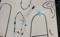 Auf einem großen Blatt Papier sind verschiedene Strecken aufgezeichnet, auf denen sich drei Mini-Roboter - sogenannte Ozobots - bewegen