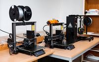 Drei 3D-Drucker auf einem Tisch in einem Labor oder Arbeitsraum, bereit für den Einsatz.