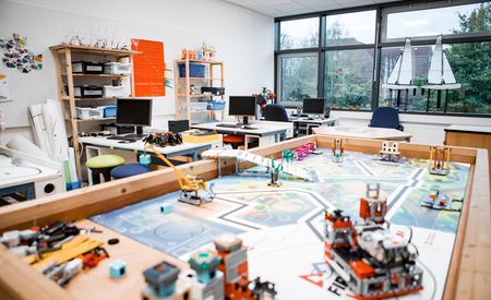 Ein Klassenzimmer mit mehreren Computern, Regalen und einem großen Tisch für Robotik- und Technikprojekte.