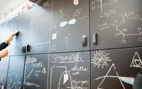 Eine Wand aus Tafeln ist mit verschiedenen wissenschaftlichen Skizzen und Formeln bedeckt, die Konzepte aus der Physik und Chemie darstellen.