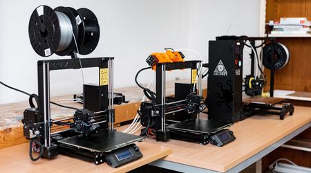 Drei 3D-Drucker auf einem Tisch in einem Labor oder Arbeitsraum, bereit für den Einsatz.